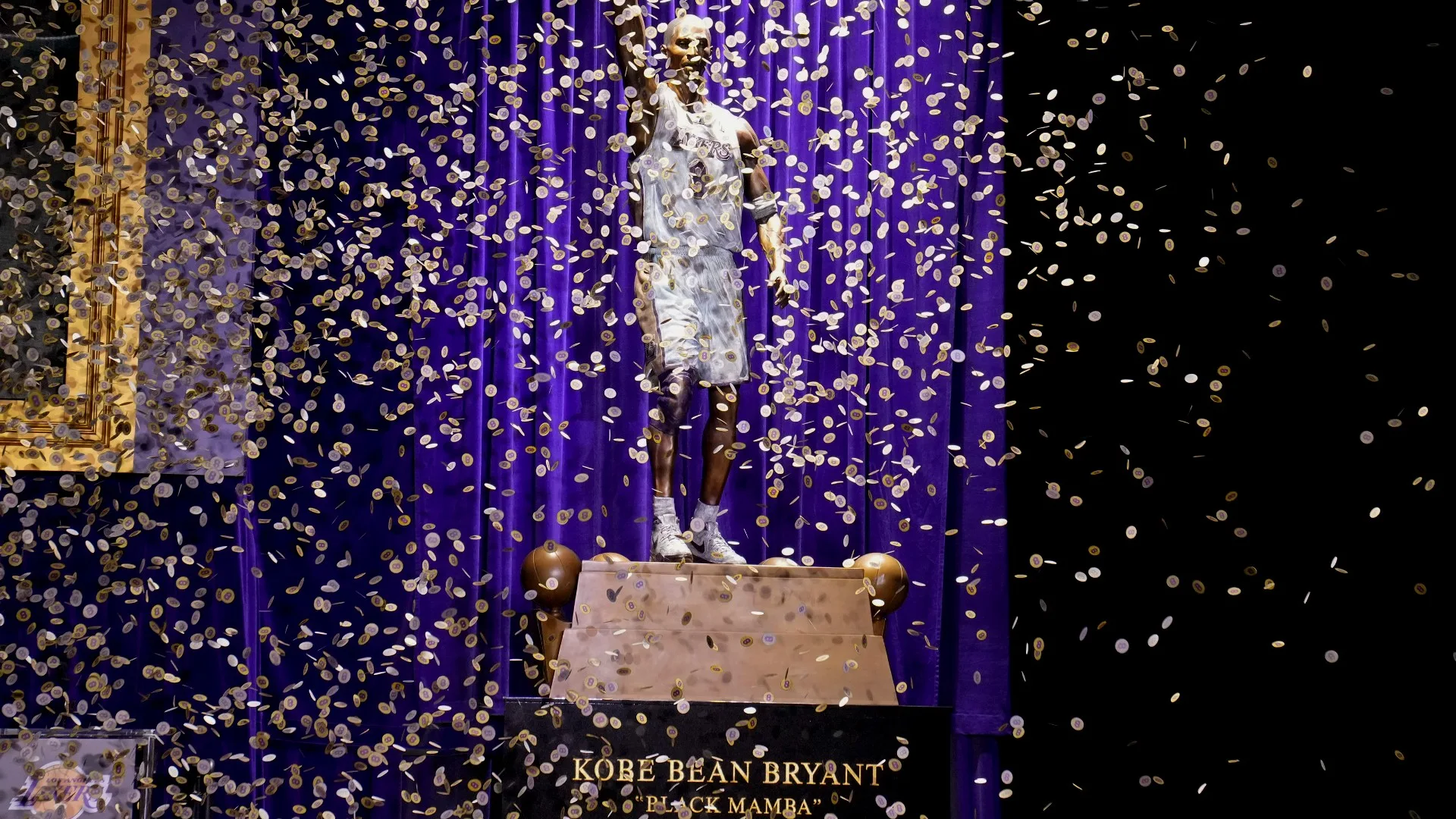 A bronze statue of Kobe Bryant in a Lakers jersey, with his right index finger raised, outside Crypto.com Arena.