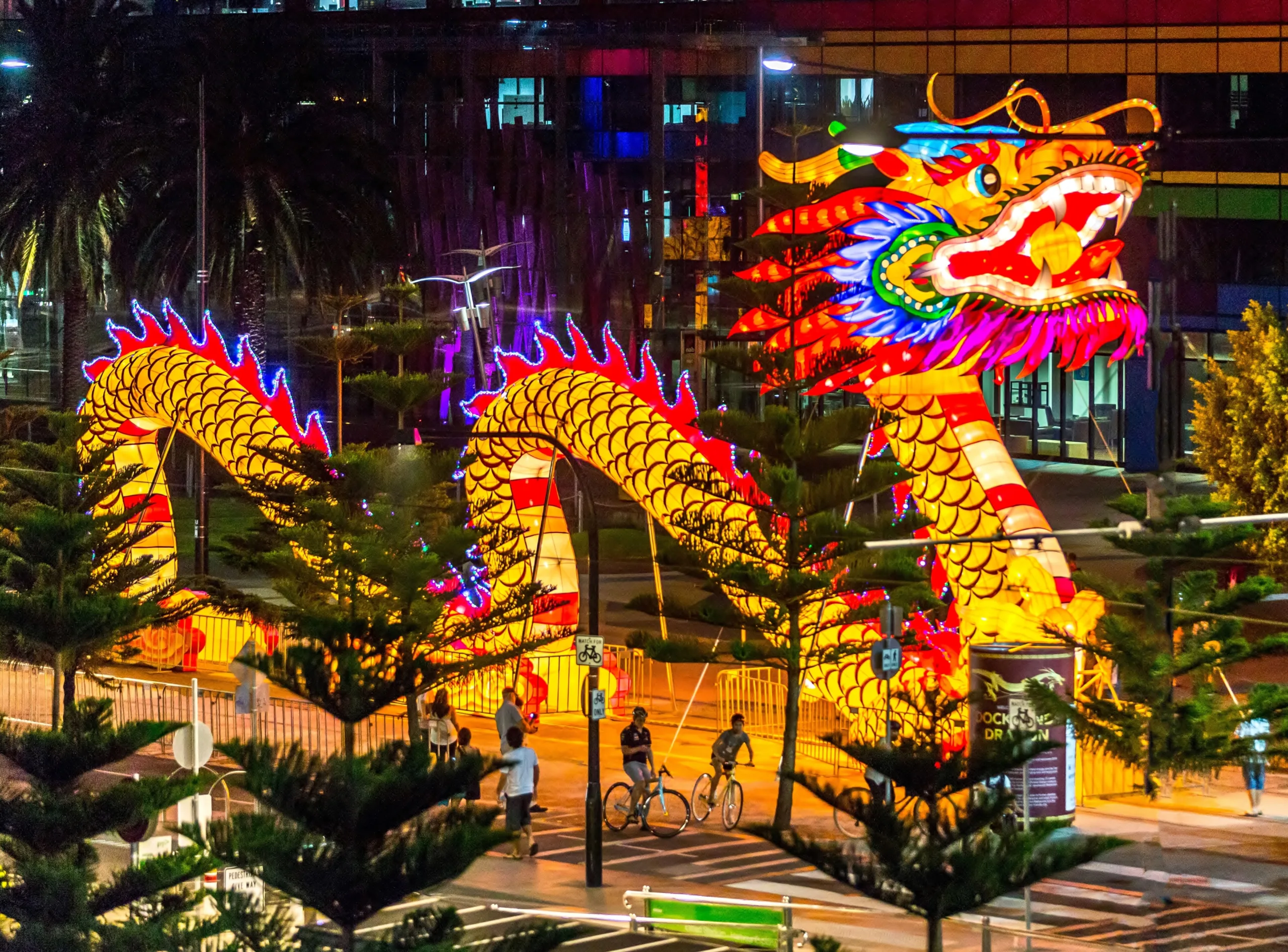 A group of people wearing traditional Asian attire celebrating Lunar New Year with dragon dance and fireworks.
